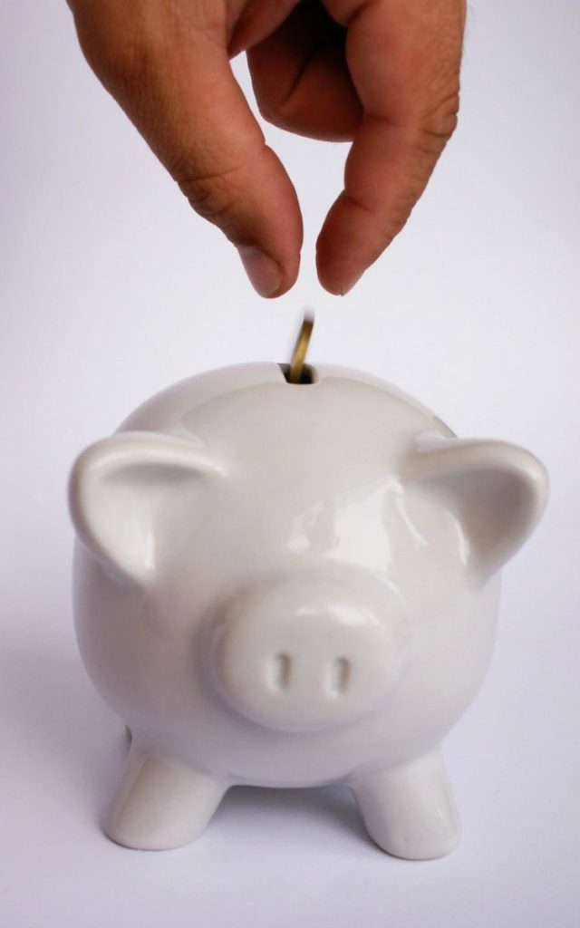 Close-up of hand dropping coin into piggy